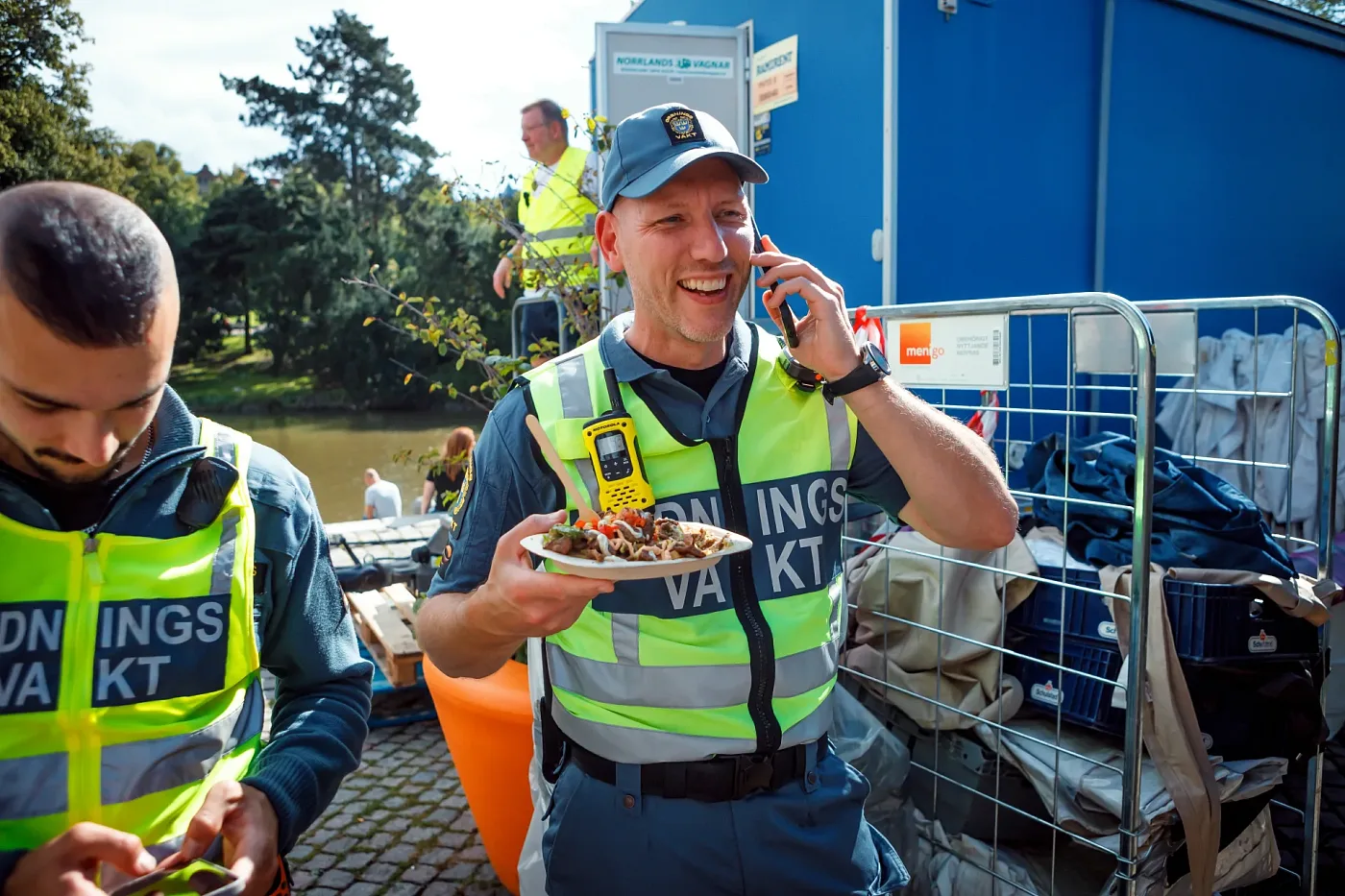 Two stewards in hi-vis vests in the festival area, one of them on the phone