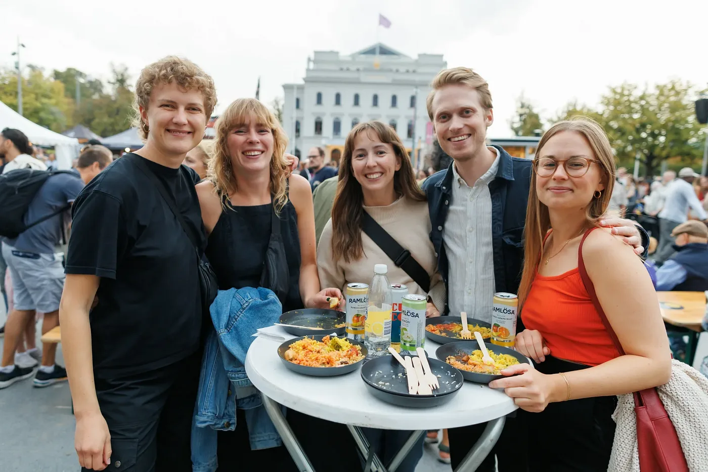Five visitors smiling at the camera at a standing table with food in the festival area