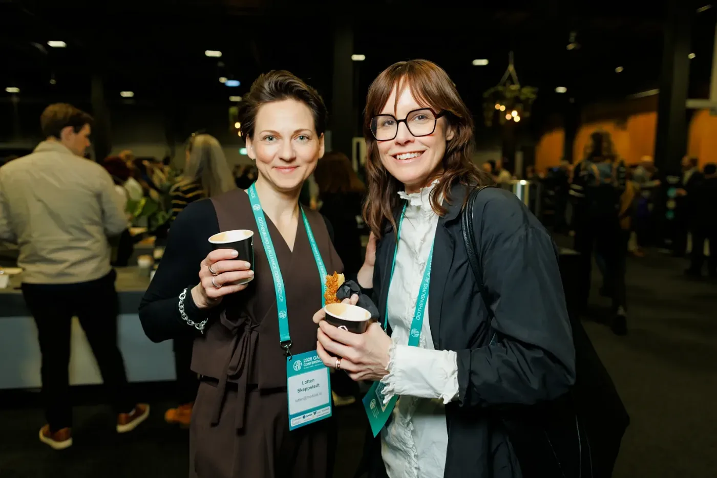 Two conference attendees with coffee smiling at the camera in the foyer