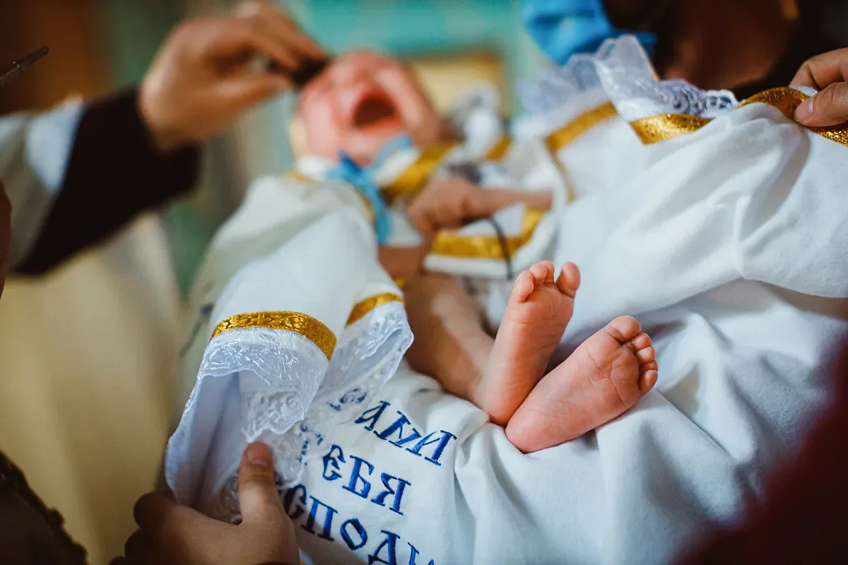 Baby’s feet in a christening gown on a towel