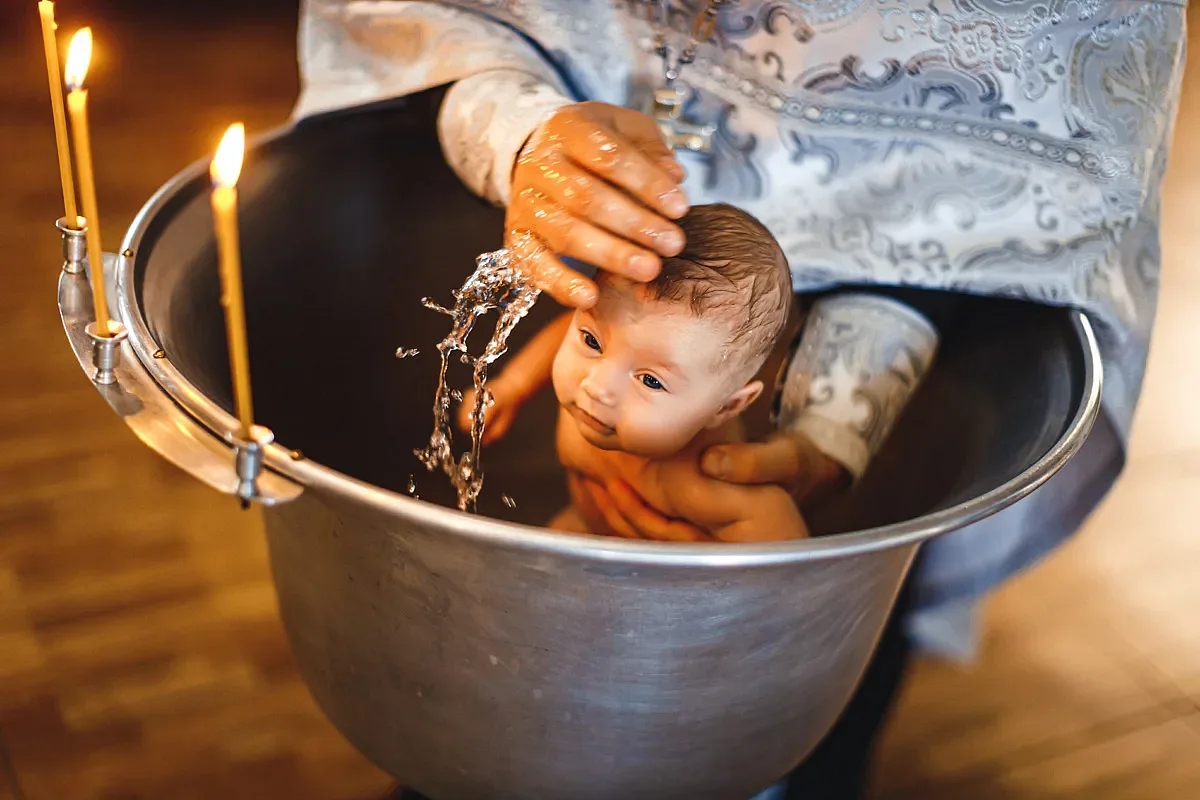 The priest immerses the baby in the font