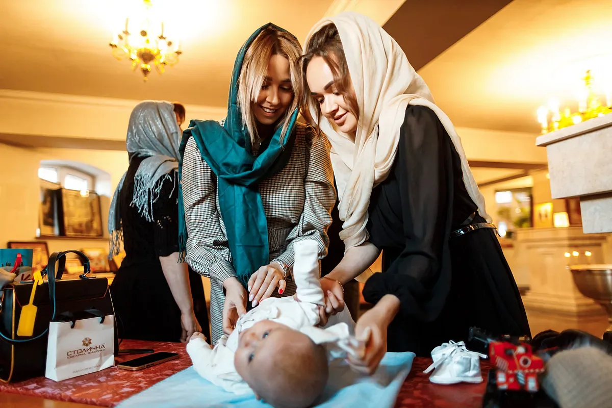 Mother and godmother dressing the baby after the font
