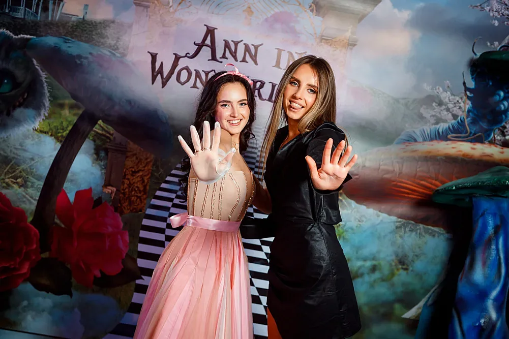 Two guests posing in front of the decorated photo wall at the party