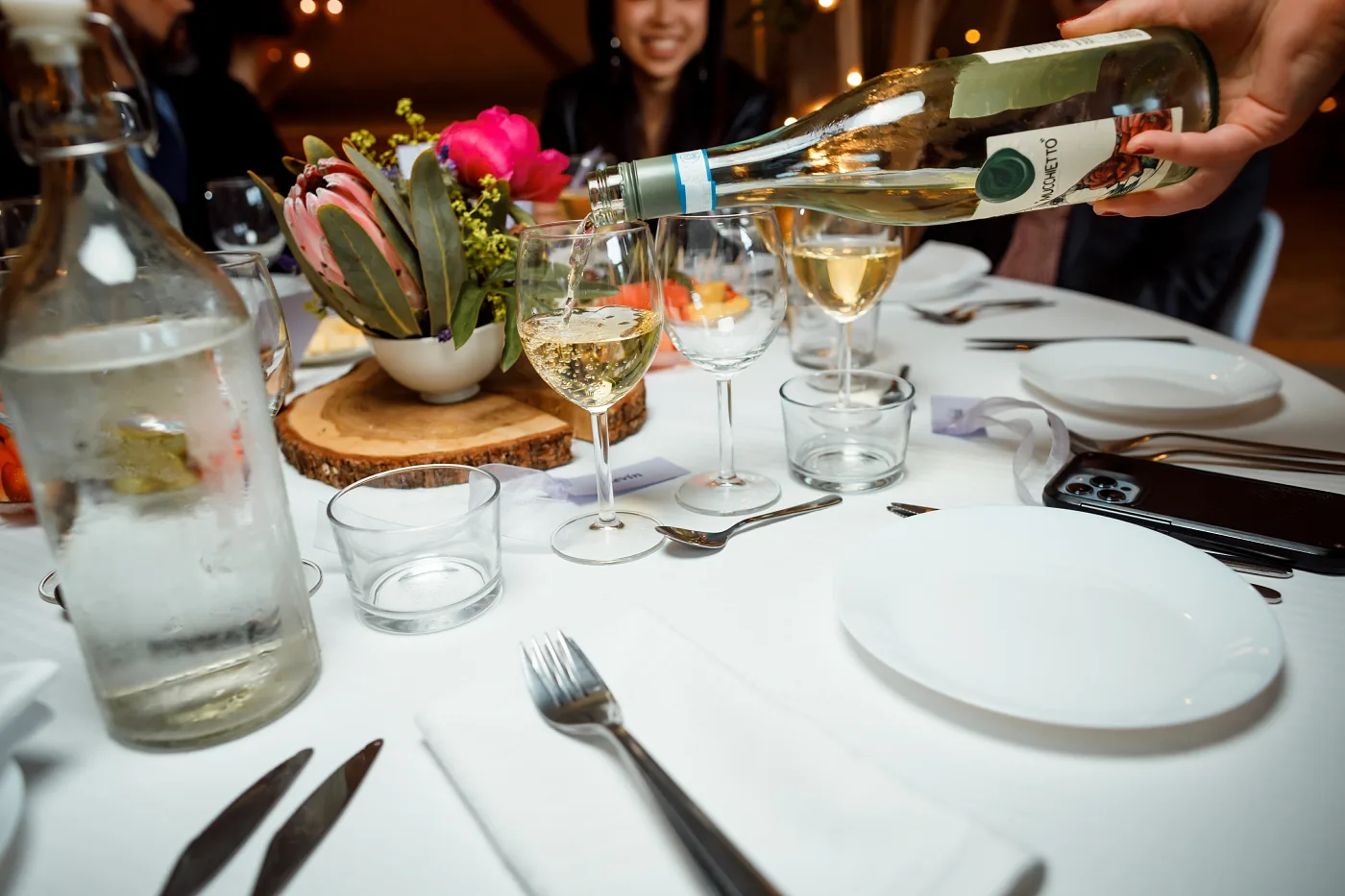Wine being poured into the glasses at the laid table with a floral centrepiece