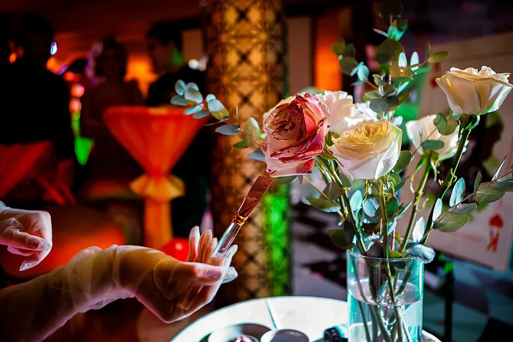 A florist in gloves arranging roses in a vase, the room behind in coloured light