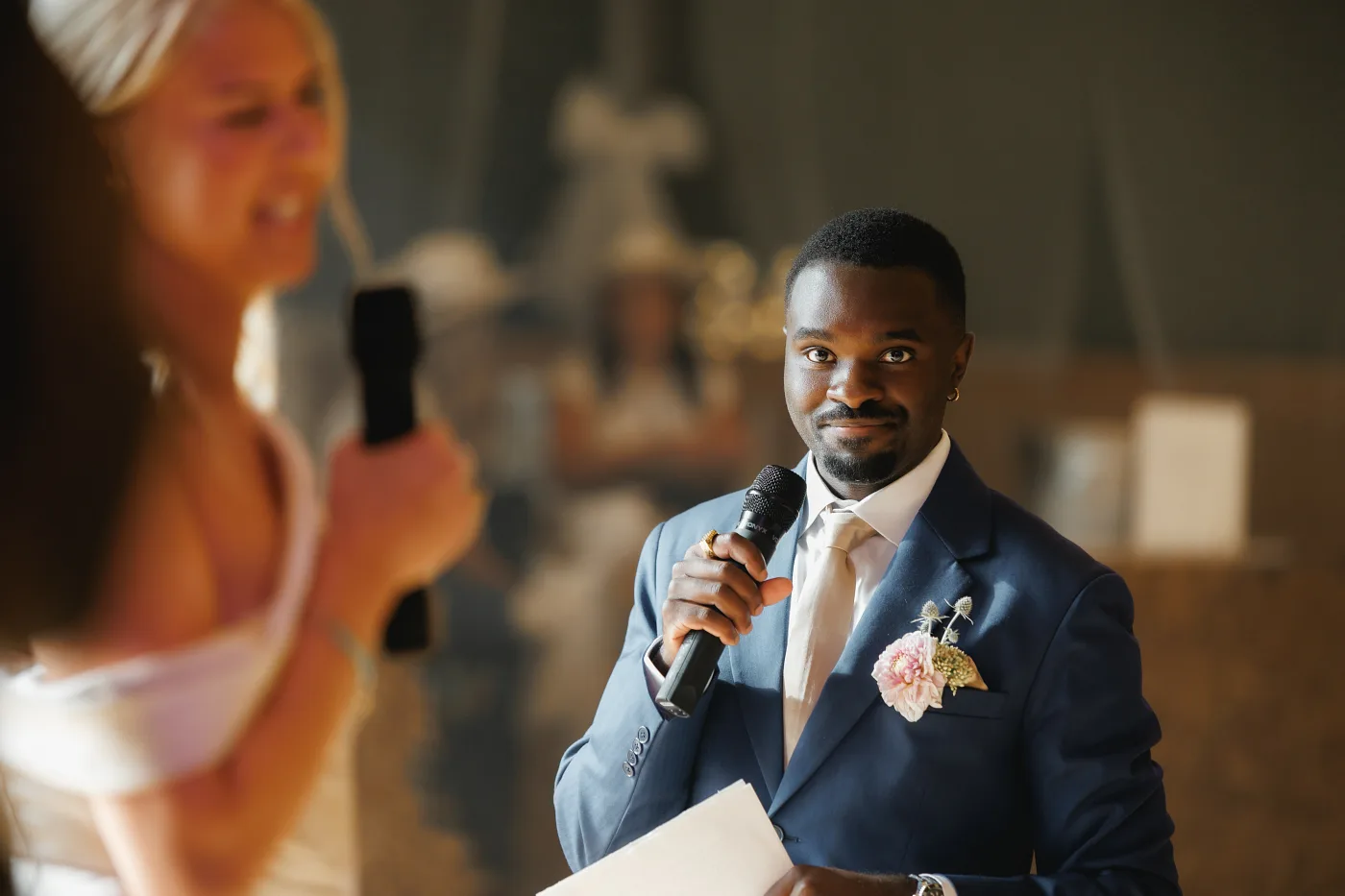 The groom answering into a microphone, the host with a mic in the foreground