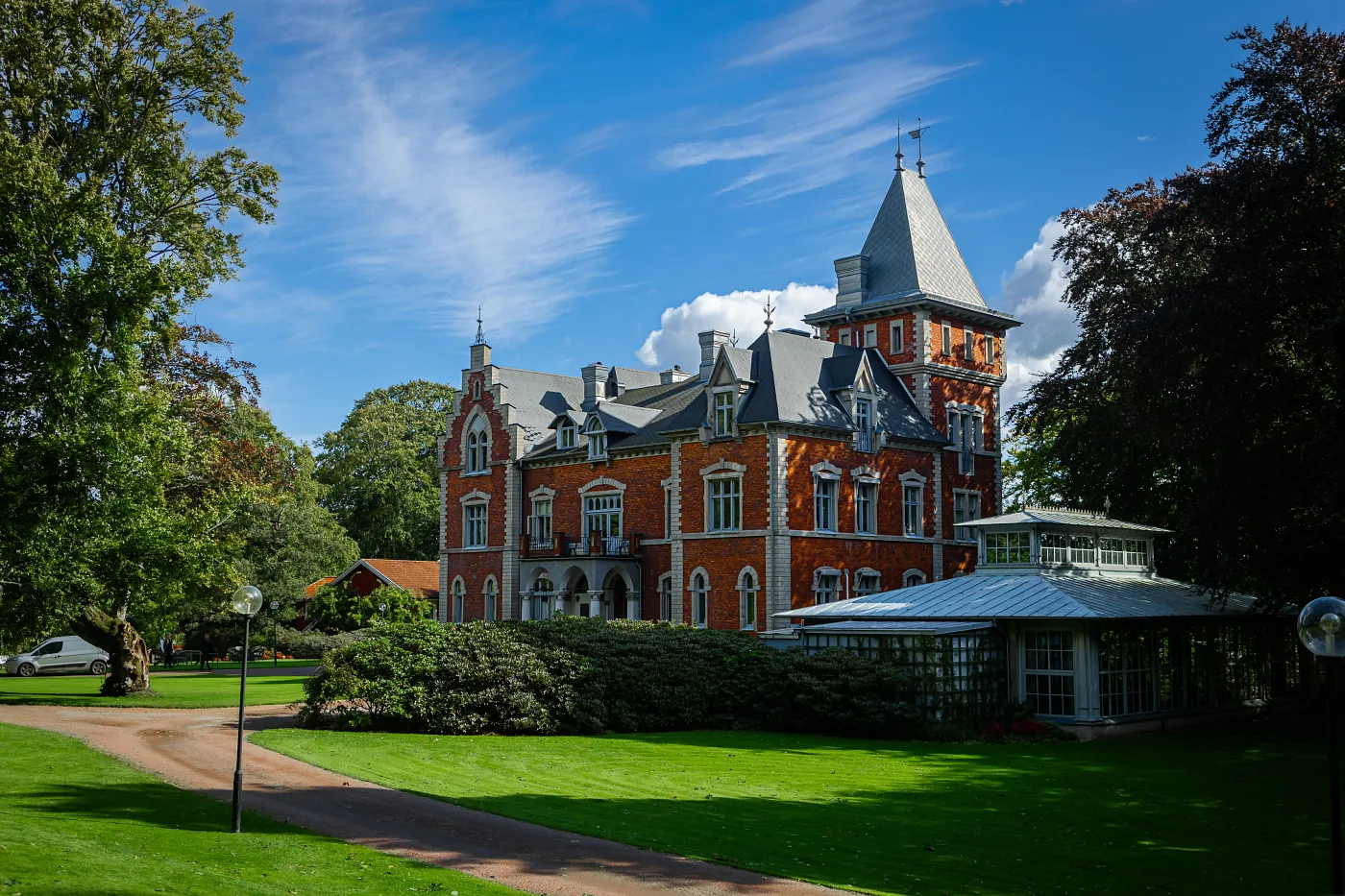 A red-brick manor with a turret and a glass orangery, lawn and gravel drive