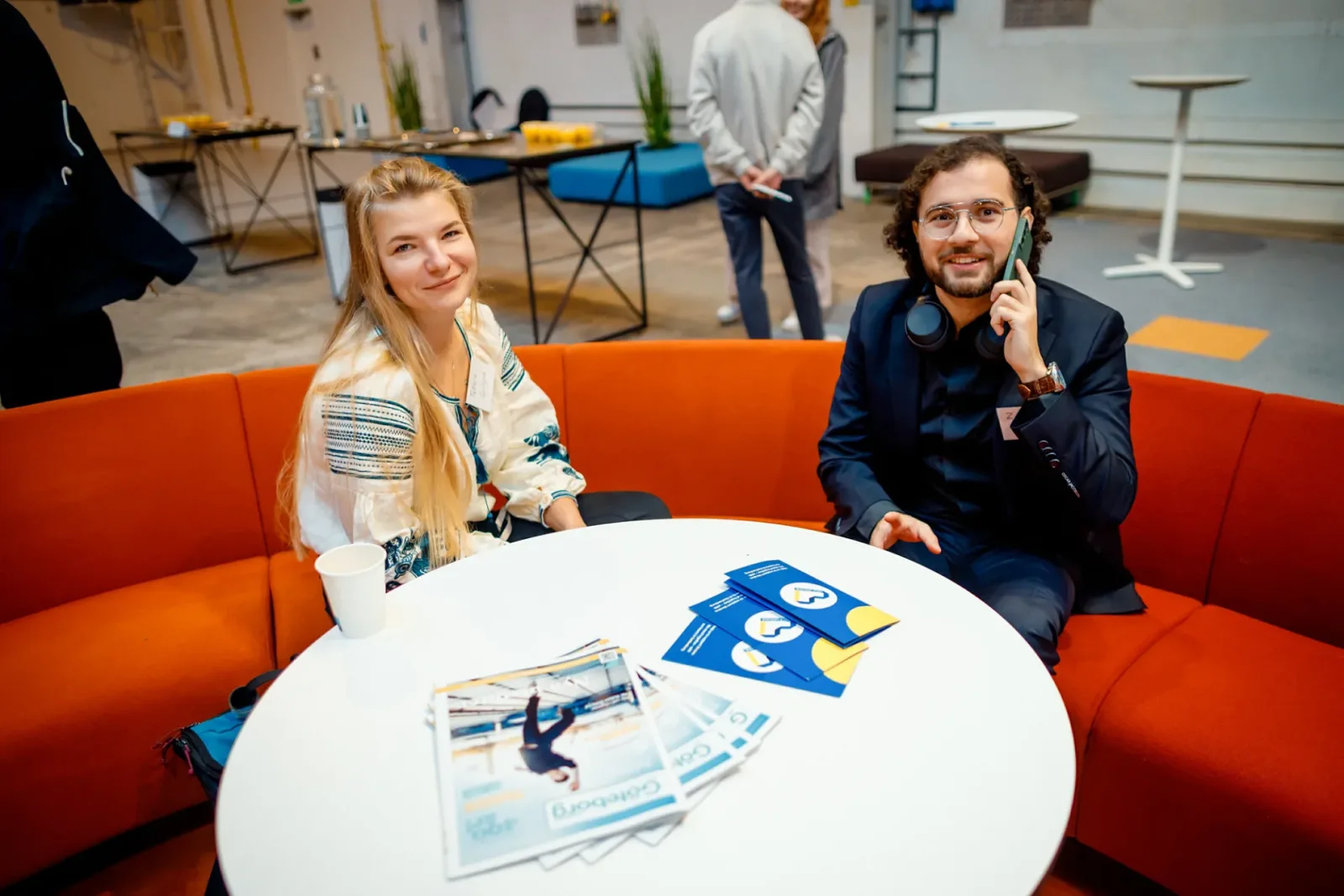 Two forum attendees on an orange sofa at a table with brochures