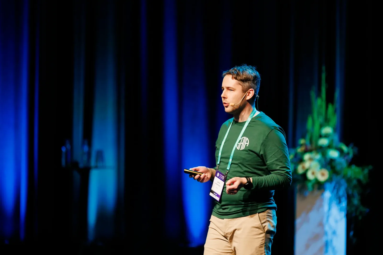 Speaker with a headset on a conference stage in front of a blue curtain