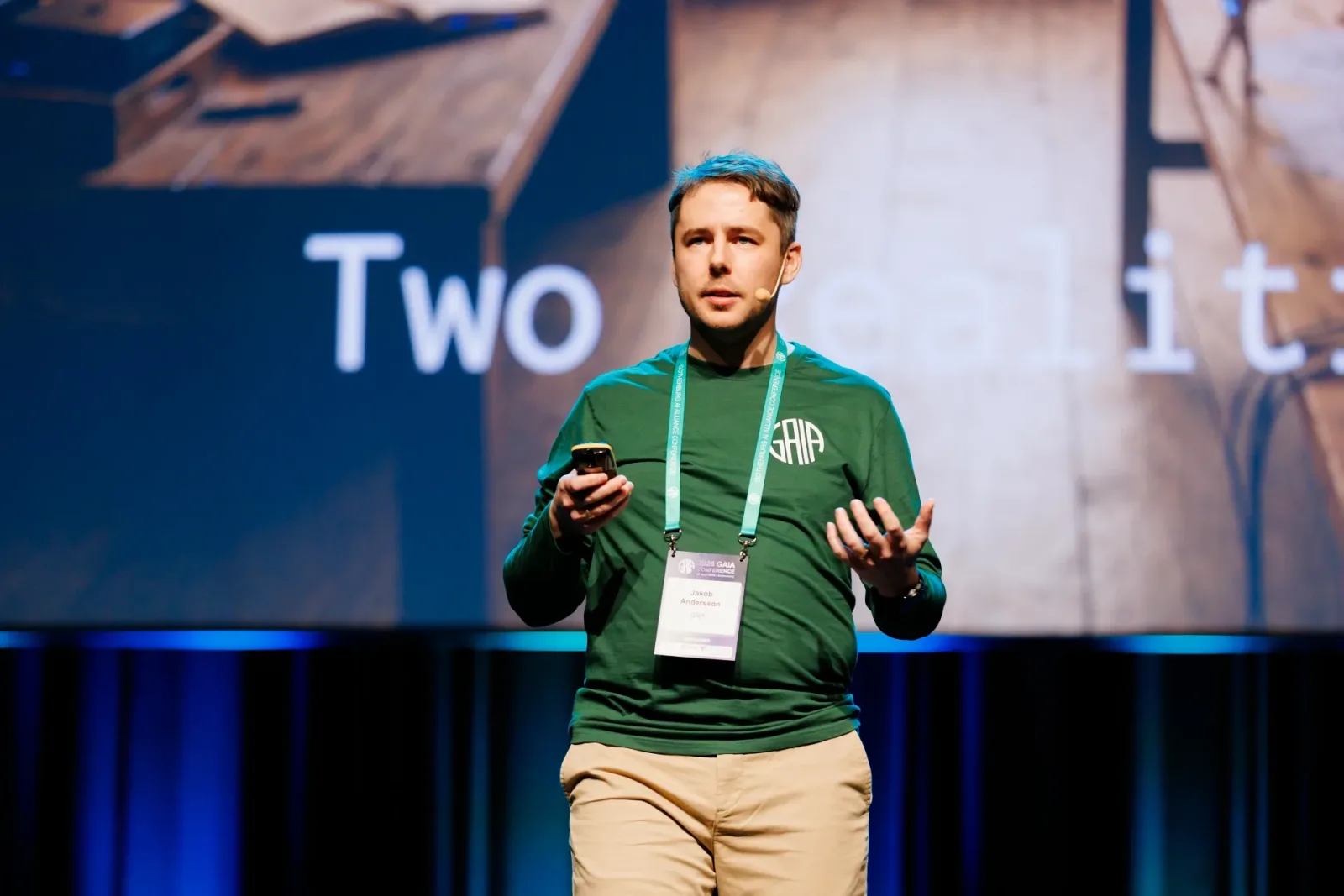 Speaker on stage in front of a large screen with a slide