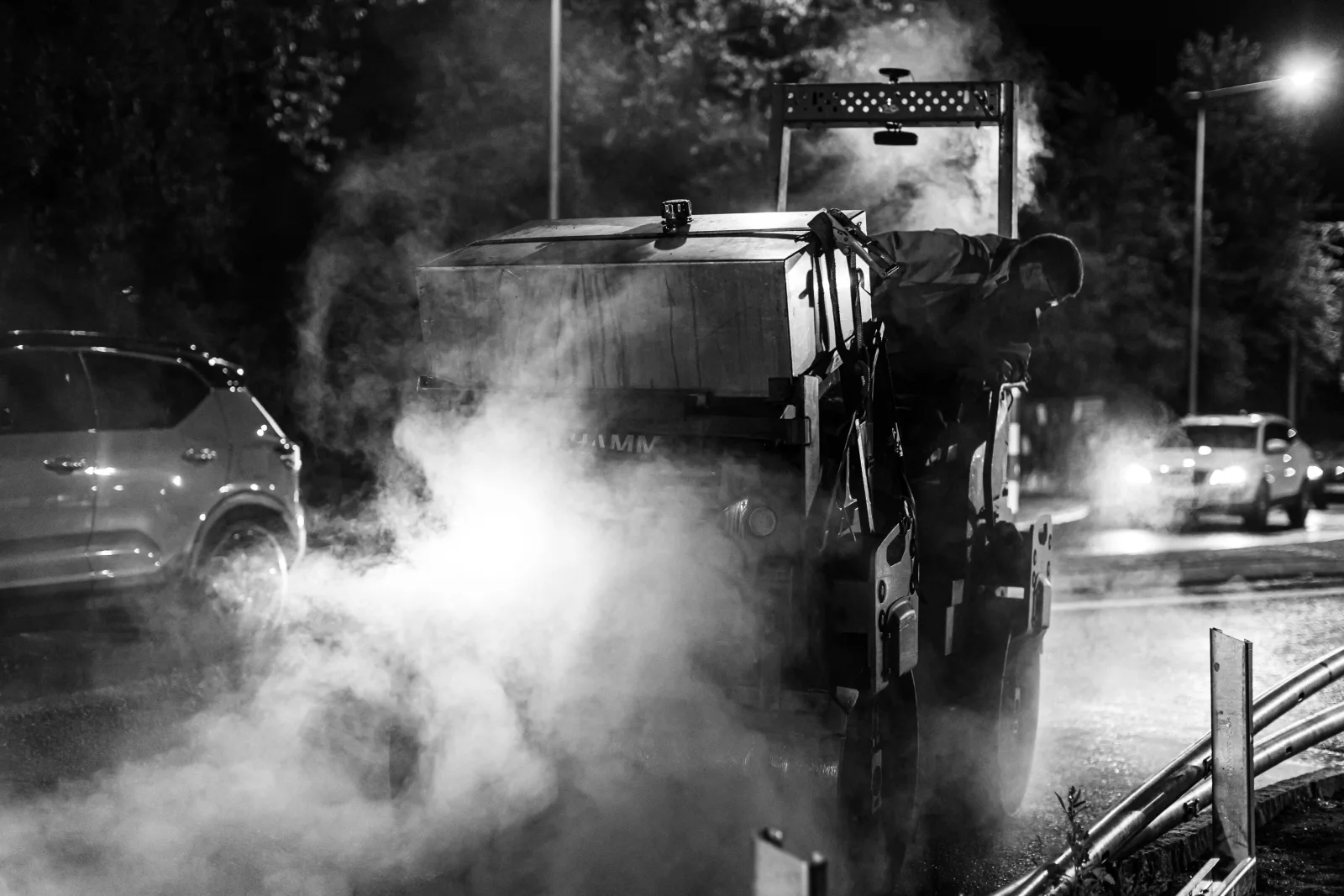 Black and white photo: a road roller in clouds of steam from hot asphalt