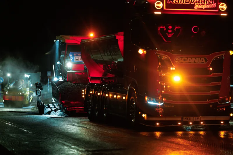 Asphalt trucks in red light on a road section at night