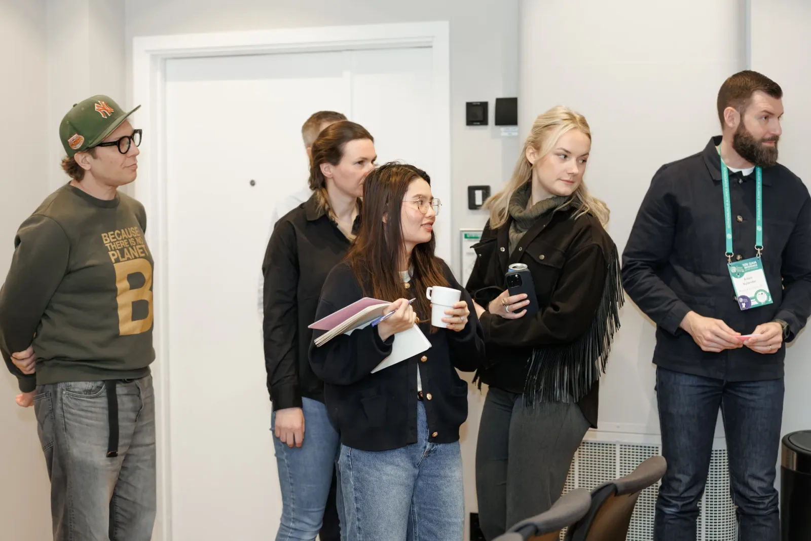 Workshop participants standing and listening, one holding a notebook