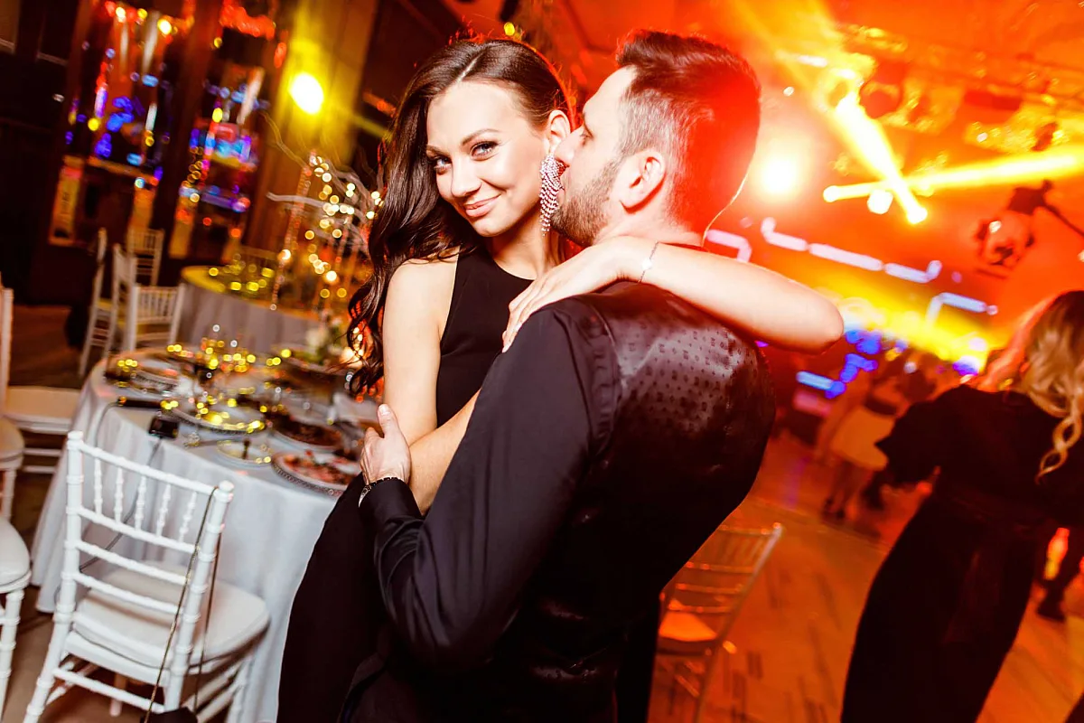 Couple laughing and hugging at a party table in orange-red light