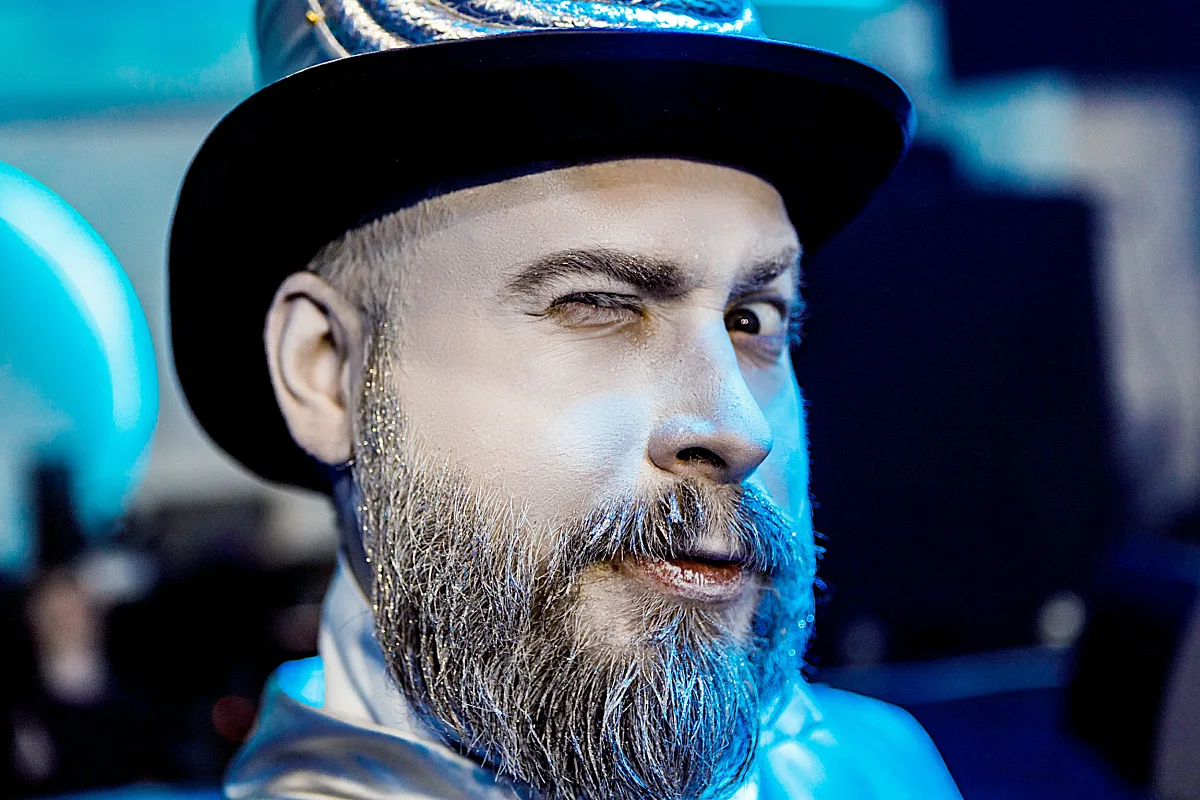 Bearded man in a glittery hat winking at the camera