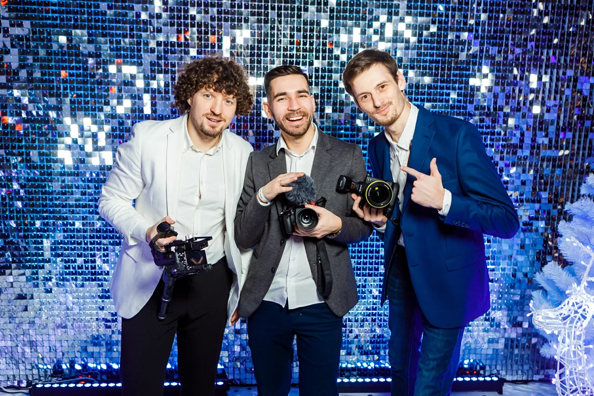 Three photographers with cameras posing in front of a sequin wall
