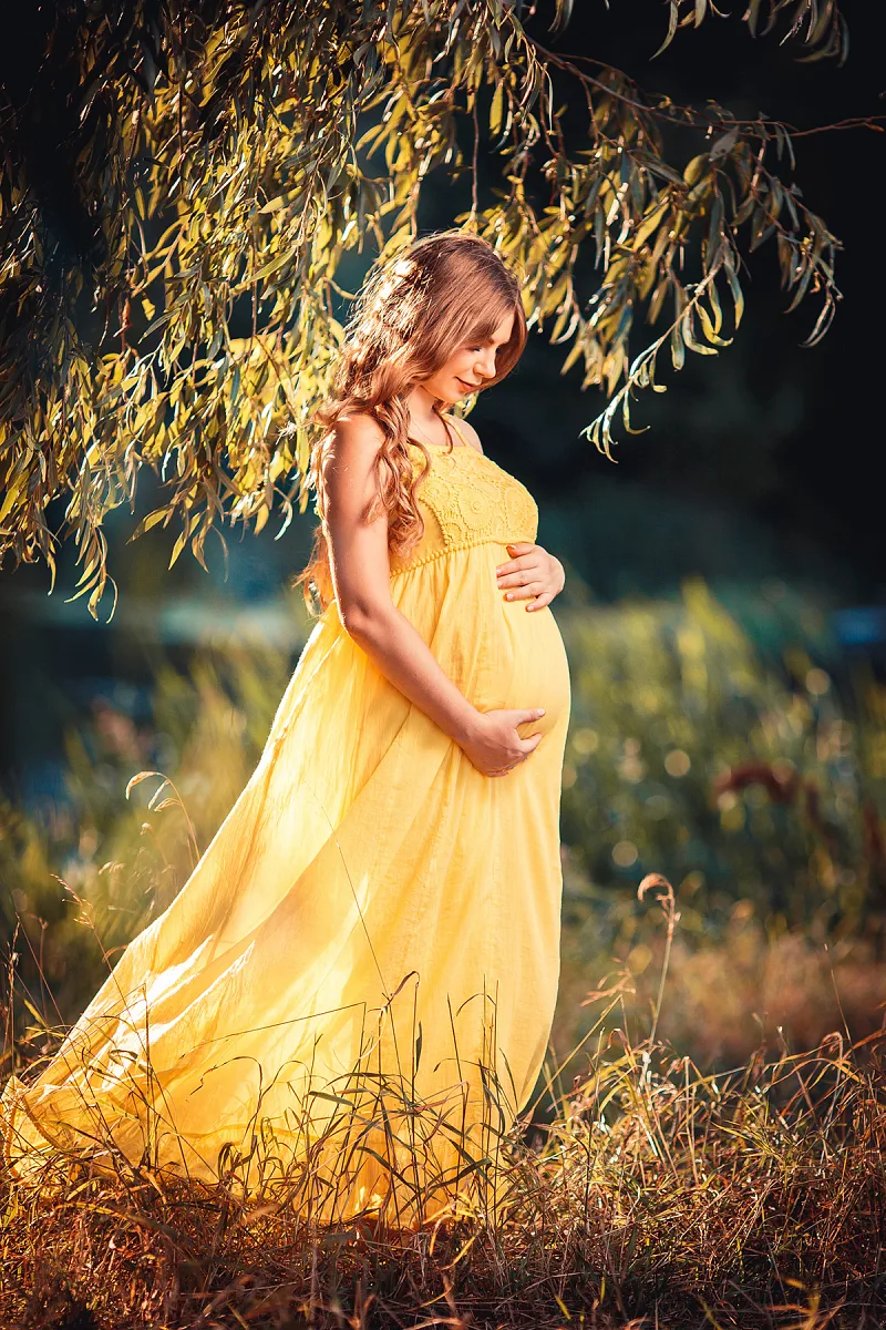 Expecting mother in a yellow dress in a field at sunset