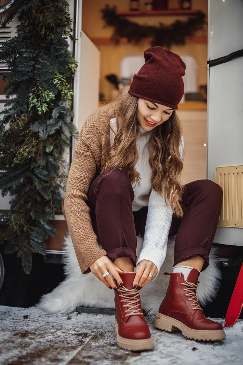 Woman in a hat and sweater lacing her boots by festive decorations