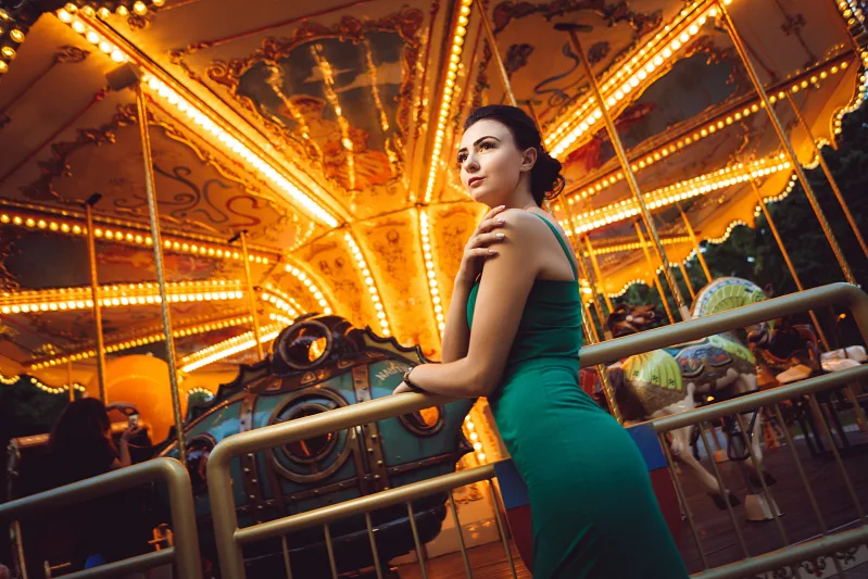 Woman in a green dress by a lit carousel in the evening