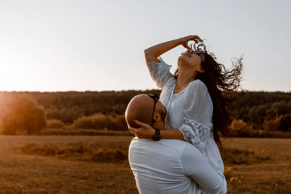 Groom lifting the bride in a field at sunset