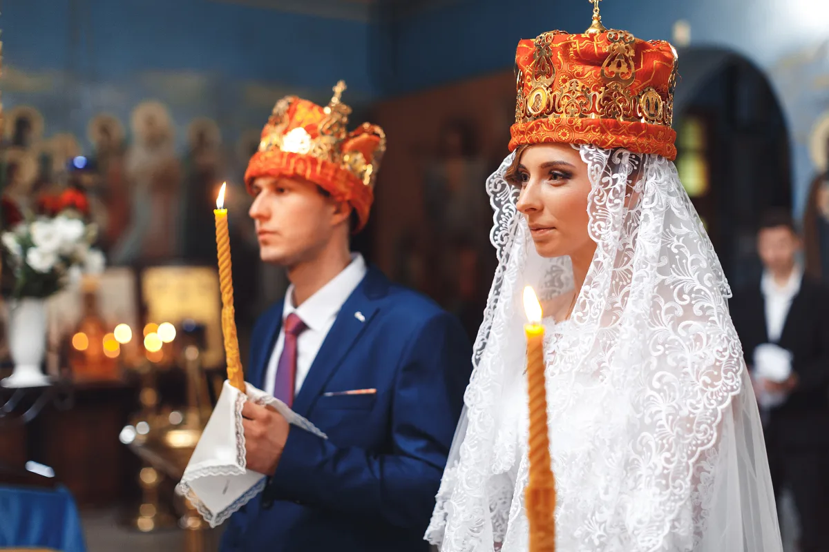 Bride and groom holding candles under wedding crowns at the church ceremony